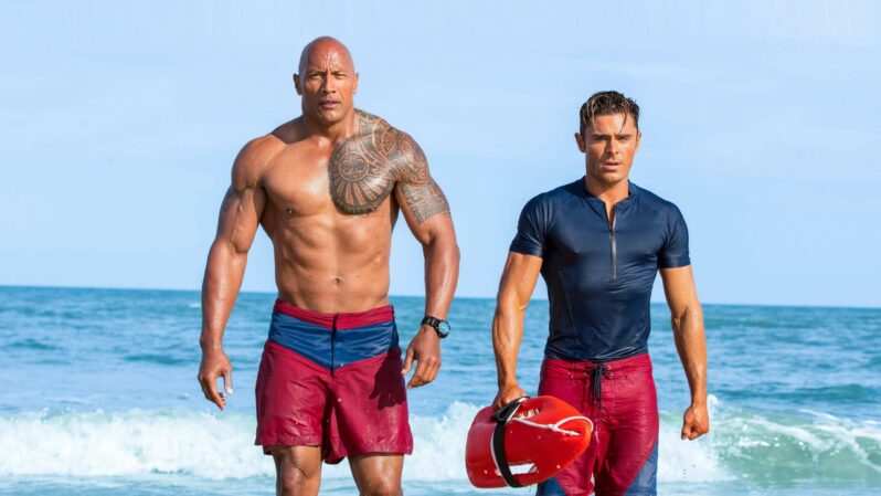 Dwayne Johnson and Zac Efron walking out of the sea in swimsuits in Baywatch (2017) now streaming on Showmax